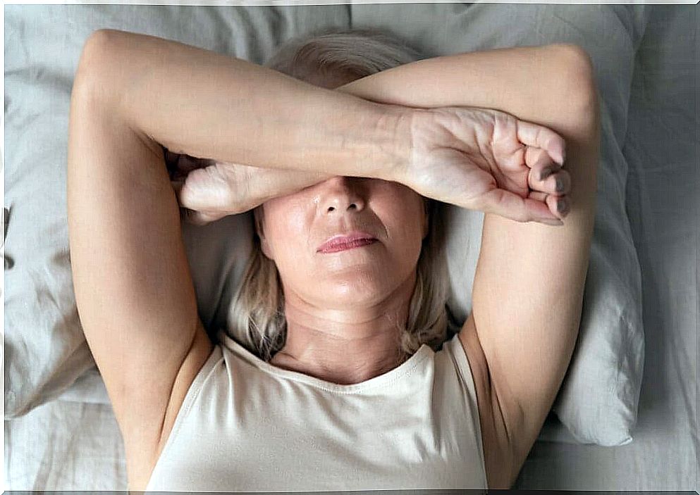 A woman lying on her bed, her arms over her eyes. 